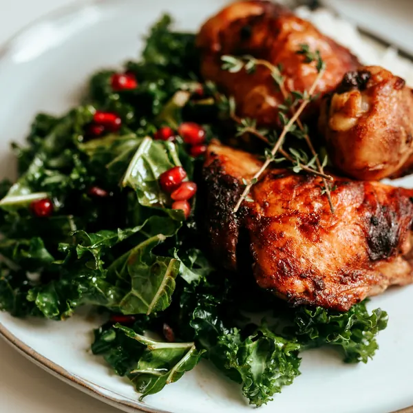 Roast chicken with leafy greens and pomegranate on a white plate